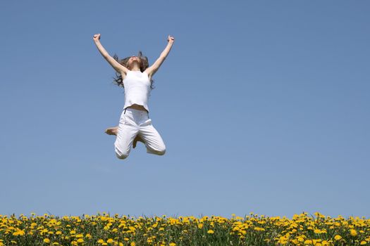 Smiling girl in a happy jump, looking up, in a flowering field.