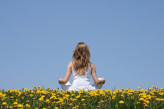 Peace of mind. Longhaired young woman in white clothes relaxing in a flowering dandelion field.