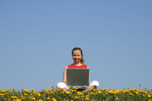 Casual young woman working with laptop outdoors, in a flowering field.