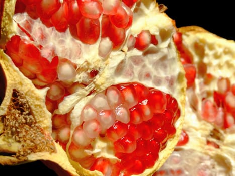 Half pomegranate fruit and its ripe seeds inside isolated on black