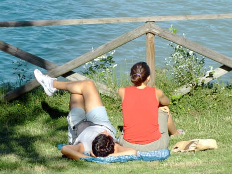 Young couple relaxing on the grass in the park, in front of the lake