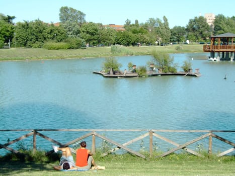 Young couple relaxing on the grass in the park, in front of the lake