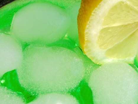 Close-up of some ice cubes and a lemon slice inside a green drink