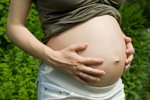 Young pregnant woman holding her stomach at summer garden