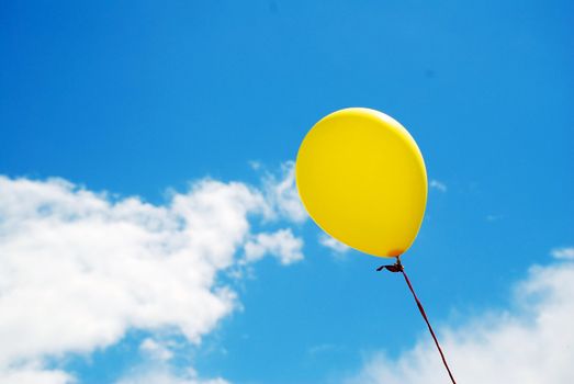 A photograph of a brightly coloured yellow balloon, under a perfect blue sky with white clouds