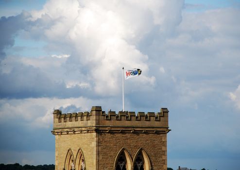 A flag reading the word HOPE flying above an old English church under a cloudy sky