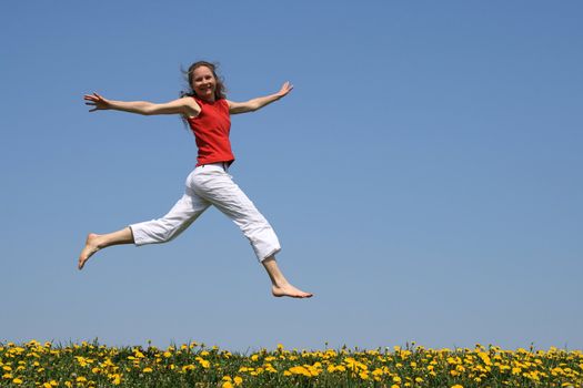 Girl in red t-shirt flying in a jump over flowering dandelion field.