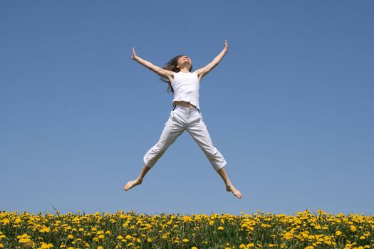 Smiling girl in summer white clothes jumping in flowering meadow.