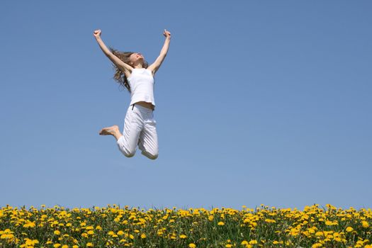 Smiling young woman in a happy jump in flowering spring field.