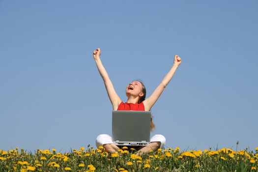 Happy young woman with laptop in a flowering spring field.