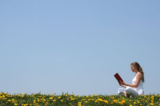 Young woman relaxing and reading a book outdoors, in a spring meadow.