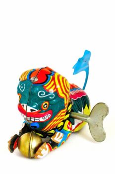 Wind-up toy dragon from China with blue tail and a golden ball in its paws, made of brightly-painted metal.  The winding key is visible in its side.