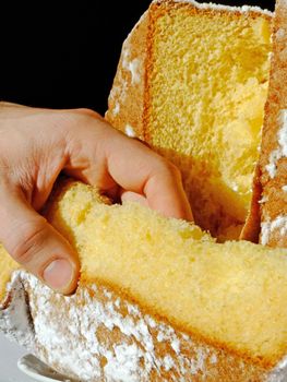Hand taking a slice of Pandoro the traditional italian Christmas cake isolated on black. It is also well known as golden cake of Verona