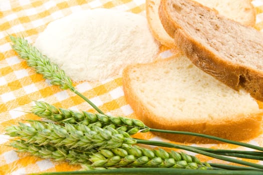 Bread, flour and green wheat on table cover.