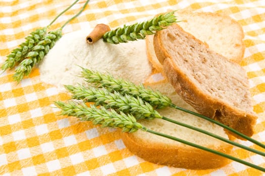 Bread, flour and green wheat on table cover.