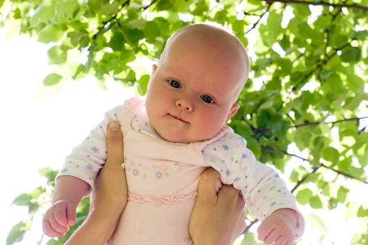 Mother holding her child against sunny leaves at summer garden