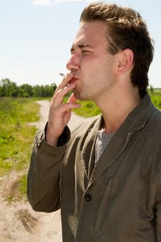 young man smokes against a rural landscape