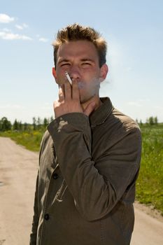 young man smokes against a rural landscape