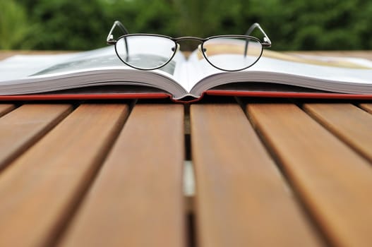 Reading glasse over open book on a wooden garden table  