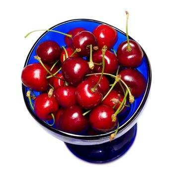 ripe fresh sweet cherries in the cup of blue glass, isolated on white