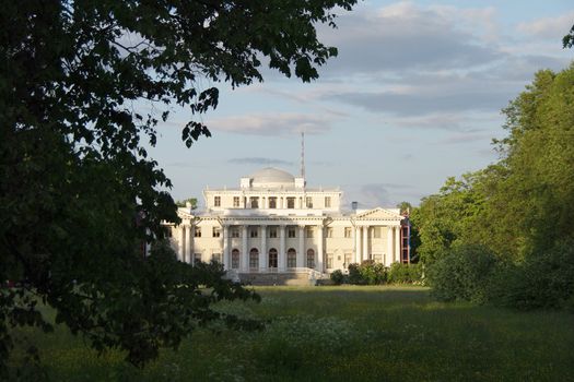 Beautiful white mansion in the sunlight behind the trees