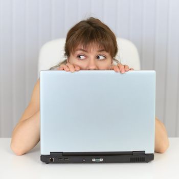 Young woman hiding behind a screen laptop