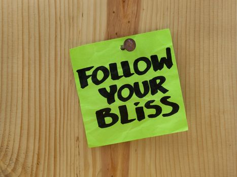 follow your bliss handwriting on a green sticky note nailed to wooden wall or plank