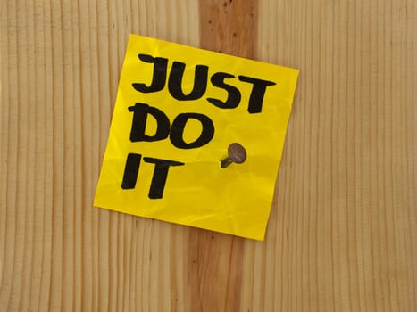 just do it, motivational reminder handwritten on yellow sticky note and nailed to wooden wall or plank