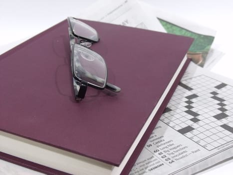 Black framed glasses lying on top of purple book and newspaper