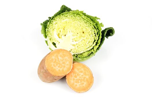 Half a raw green cabbage with a sweet potato cut in half on a reflective white background