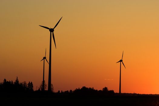 Three windturbines against dramatic sunset producing environment friendly energy