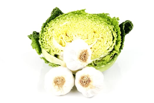 Half a raw green cabbage with raw white garlic bulbs on a reflective white background