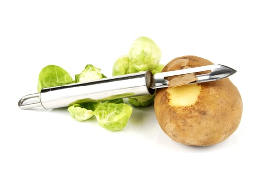 Small brown raw potato with chrome peeler and peeled green sprouts on a reflective white background