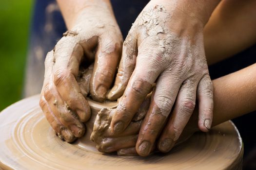 A potters hands guiding a child hands to help him to work with the ceramic wheel