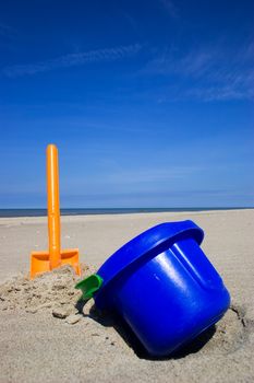 Orange plastic spade and blue bucket in the sandy seashore