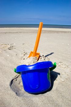 Orange plastic spade and blue bucket in the sandy seashore