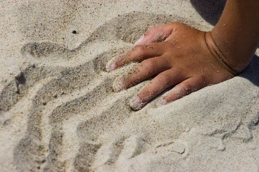 Kids hands playing with the sand on the beach.