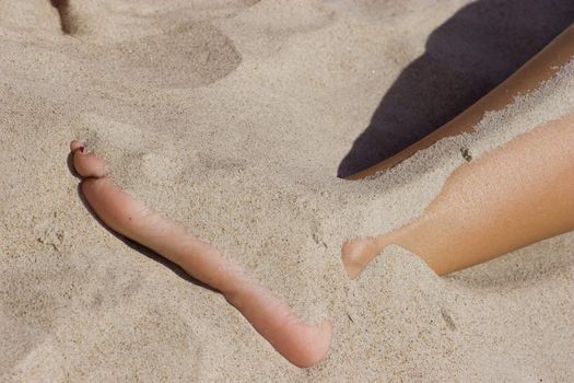 Leg of young woman in the sand on the beach.