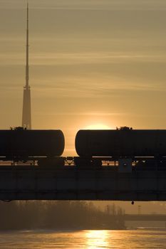 Silhouette of freight tank wagons on a bridge. Morning Sunrise. In background TV tower