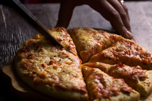 Cutting in pieces cheese pizza on wooden plate