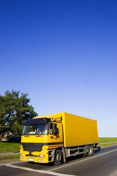 Yellow truck on asphalt road. Large blue sky with place for copy text.