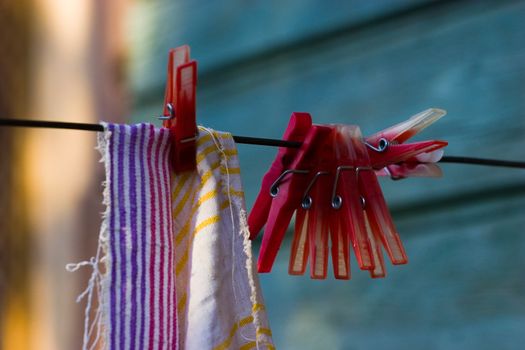 Red plastic clothespins and towel on a black washing line, selected focus on clothespins with soft and diffused background.