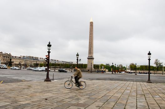 Young parisian riding with bicycle near Obelisk at the Place de la Concorde, Paris. Early morning. Motion blur.