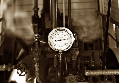 sepia image of machinery under pressure gauge lets out steam