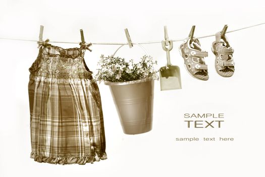 Little girl clothes and toys on a clothesline against white background/ Sepia tone