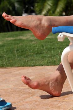 Woman feet resting on the chair by the pool