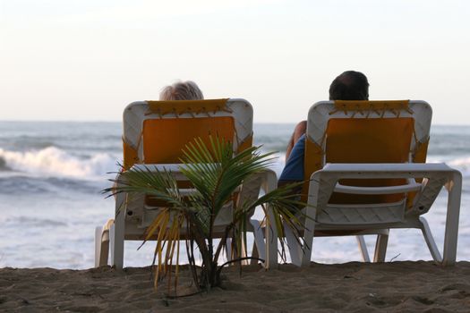 couple lying in chaise longues on the beach by hotel