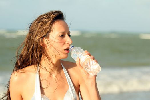 Woman drinking water from bottle on the beach 