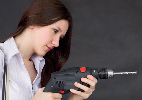 Female student learns to use a drill on a black background