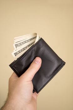 A hand holding a wallet full of cash isolated over a gold background